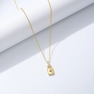 Détail du pendentif cadenas doré avec pierre centrale rouge et éclats de zircons blancs