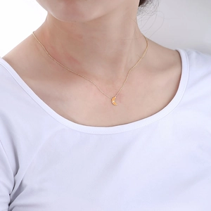 Detail of orange enamel moon pendant with a tiny diamond on a gold chain necklace