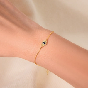 Goldenes Evil-Eye-Armband mit blauem Stein am Handgelenk mit weichem Strickhintergrund