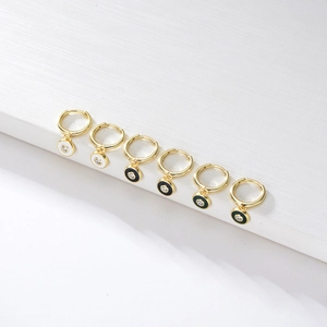 Macro detail of gold C-shape hoop earrings with black and white enamel dripping and zircons