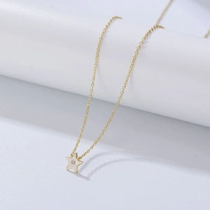 Détail macro d'un collier pendentif étoile dorée avec émail blanc et petite pierre zircon