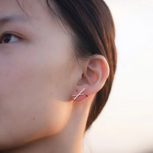 Close-up of golden S925 silver X-shaped crisscross stud earrings with zircon on woman's ear