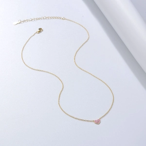 Détail macro du fermoir mousqueton doré et du pendentif cœur en émail rose