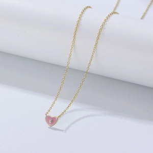 Détail d'un pendentif cœur en émail rose avec pierre scintillante sur chaîne fine dorée