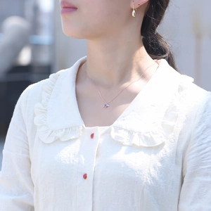Detail of rose gold angel wing necklace with a blue heart-shaped stone on a model