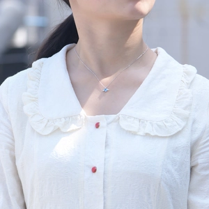 Detail of silver angel wing necklace with heart-shaped blue stone on model neck
