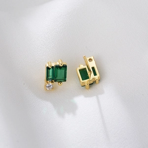 Macro detail of geometric emerald-cut green stone earrings on white silk fabric