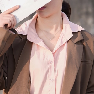 Detail view of gold evil eye opal necklace worn by a woman with pink shirt and brown blazer