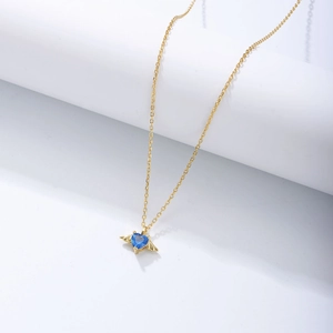 Close-up of gold angel wing necklace with a heart-shaped blue gemstone pendant