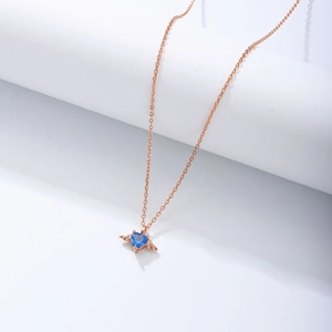 Macro shot of rose gold angel wing pendant with blue heart zircon on white stand