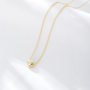 Detailed view of a 3D gold heart pendant on a delicate chain over white silk fabric