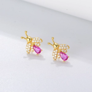 Macro shot of gold bee earrings with white zircons and pear-cut pink gemstones
