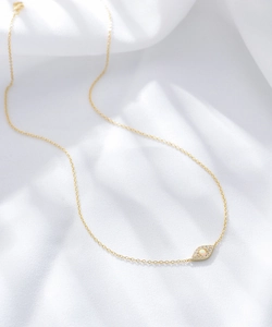 Detail of gold evil eye necklace with iridescent opal and zircons on white silk