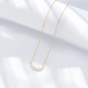 Macro detail of gold angel wing pendant with pavé set cubic zirconia on white silk
