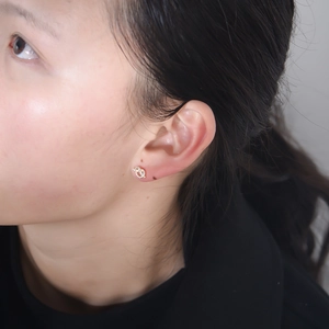 Detailed view of silver knot stud earrings with white zircons on a model's ear