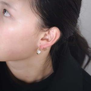 Elegant C-shaped gold pearl earrings for women showing a minimalist side view on a model