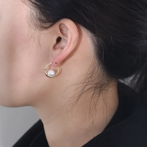 Close-up of elegant gold C-shape irregular hoop earring with pearl on model's ear