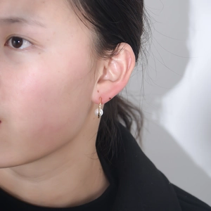 Close-up of a minimalist C-shaped gold stud earring with a white pearl on an earlobe