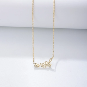 Détail macro du pendentif wish doré sur un collier à maillons minimaliste