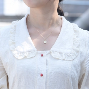 Close-up of a minimalist gold square pendant with an eight-pointed star worn on the neck