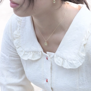 Detailed view of a gold square starburst pendant necklace with zircon on a white blouse