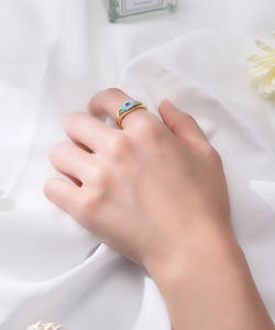 Vue détaillée d'une bague dorée avec pierre coeur rose et émail bleu portée à la main