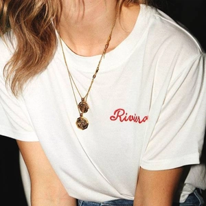 Gros plan du collier pendentif pièce d'or vintage porté sur un t-shirt blanc brodé