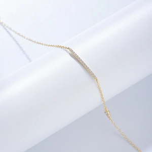 Detailed view of a gold bar necklace with white zircons on a white cylindrical stand