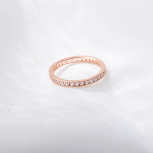 Detail of rose gold eternity band with micro-paved cubic zirconia on white silk