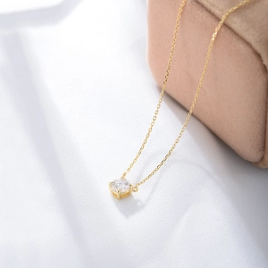 Detail einer runden Zirkonia-Halskette auf goldener Kette über weißem Stoff