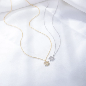 Close-up of gold and silver hexagram pendants with micro-pave zircons on soft fabric