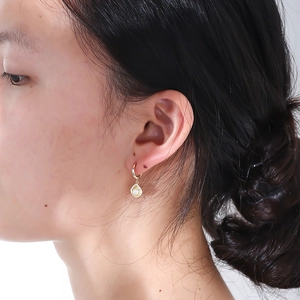 Close-up of golden shell-shaped pearl earrings with sparkling diamond accents on model