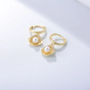 Close-up of gold shell earrings featuring white pearls and sparkling crystal details