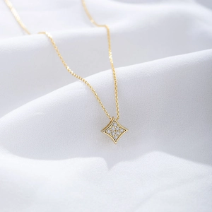 Macro view of a gold square zircon pendant on a fine chain over silk fabric