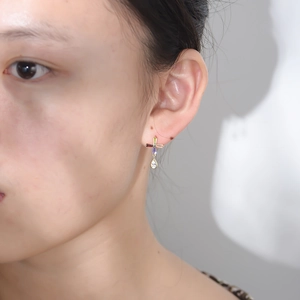 Detail of cross earring with colorful rectangular zircons and a teardrop pendant