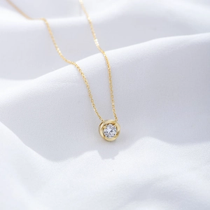 Close-up of golden sterling silver necklace with sparkling round zircon on white silk