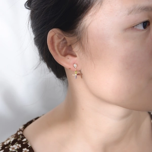 Close-up of a colorful zircon cross earring worn by a model in a gold setting
