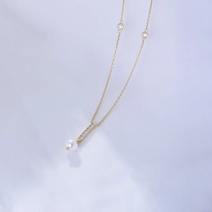 Detailed macro of gold tassel pendant featuring pavé zircons and a round white pearl