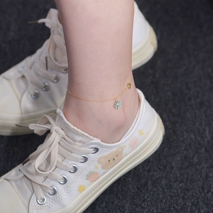Detail of gold ankle chain with blue enamel daisy and bow charm worn on the ankle