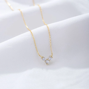 Detail of a gold heart pendant with three sparkling zircons on a white silk background
