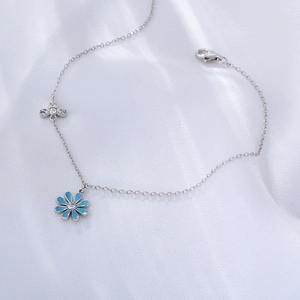 Close-up of silver anklet with blue daisy and crystal flower pendants on white silk