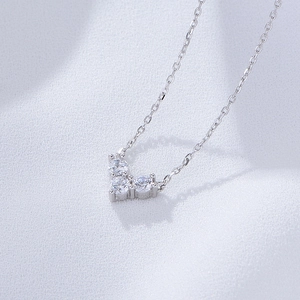 Macro view of silver heart pendant necklace with three white zircons on textured fabric