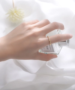 Détail d'une bague dorée torsadée avec diamants portée en tenant un flacon de parfum