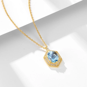 Minimalistische Goldkette mit hexagonalem Blautopas-Anhänger und Kristall-Halo auf weißem Sockel