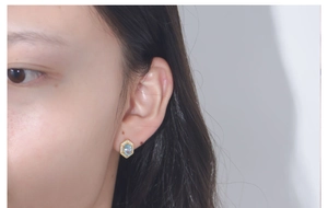 Detail of geometric blue topaz earring with gold hex frame on model's ear