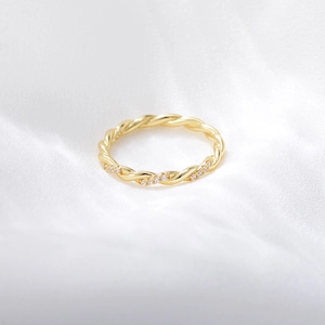 Détail de la bague torsadée dorée ornée de diamants sur un fond en soie blanche