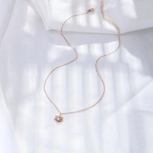 Détail du collier soleil en or rose avec opale centrale sur tissu en soie blanche