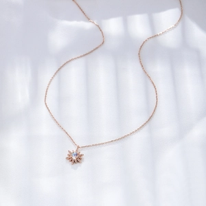 Détail du collier tournesol en or rose avec opale et cristaux sur un tissu blanc doux