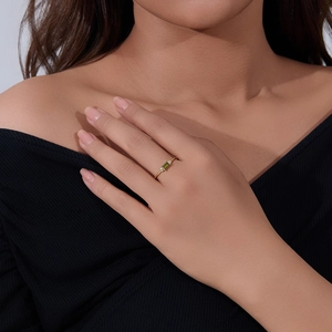 Close-up of minimalist gold ring with emerald-cut green stone on a finger