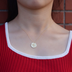 Dettaglio di una collana vintage con ciondolo a moneta ape dorata su catena sottile